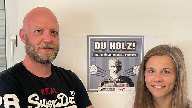Unser Bild zeigt Alexander Pf&uuml;lb mit seinem ersten Interview-Gast Annika Graser vor dem Logo des Rh&ouml;ner Fu&szlig;ball-Podcasts "Du Holz".  Foto: Sebastian Schmitt