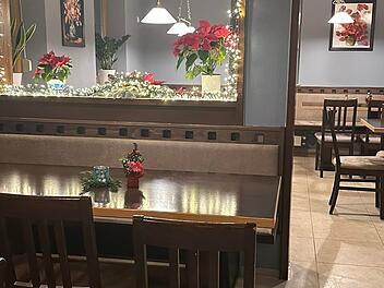 Gem&uuml;tliches Restaurant mit h&ouml;lzernen Sitzb&auml;nken und Tischen, weihnachtlich dekoriert mit Lichterketten und roten Blumen. Dezente Beleuchtung schafft eine einladende Atmosph&auml;re.