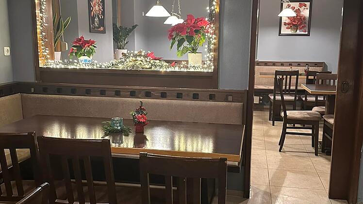 Gem&uuml;tliches Restaurant mit h&ouml;lzernen Sitzb&auml;nken und Tischen, weihnachtlich dekoriert mit Lichterketten und roten Blumen. Dezente Beleuchtung schafft eine einladende Atmosph&auml;re.