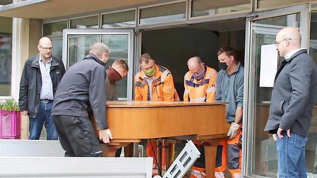 Die Mitarbeiter des Bauhofs tragen den schweren Fl&uuml;gel in die neue Musikschule. Viel schwieriger war es, ihn aus der Zehntscheune zu holen. Schulleiter Thomas Reu&szlig; (links) und B&uuml;rgermeister Michael Kastl (rechts) haben den Umzug seit Wochen vorbereitet.  Foto: Thomas Malz