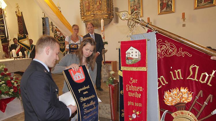 Der Vorsitzende der Patenwehr aus Kauernhofen, Sebastian Grasser (links), heftet das Fahnenband an. Es soll den starken Zusammenhalt der beiden Wehren symbolisieren. Foto: Mathias Erlwein
