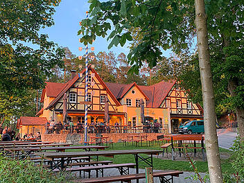 Ein malerischer fr&auml;nkischer Bierkeller bei Sonnenuntergang, umgeben von B&auml;umen. Es gibt Holzb&auml;nke und Tische im Freien, mit einem traditionellen Geb&auml;ude im Hintergrund.
