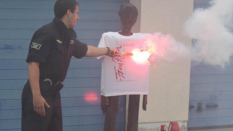 Ein Beamter der Bereitschaftspolizei zeigt, wie gefährlich die heiße Flamme eines Bengalos sein kann. Mühelos verbrennt sie das T-Shirt einer Puppe. Foto: Groscurth