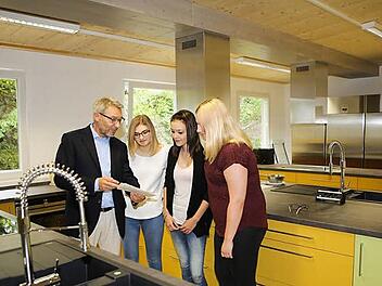 Schulleiter Wilhelm Schmitt zeigt Schülerinnen die neue Schulküche. Foto: RiegerPress