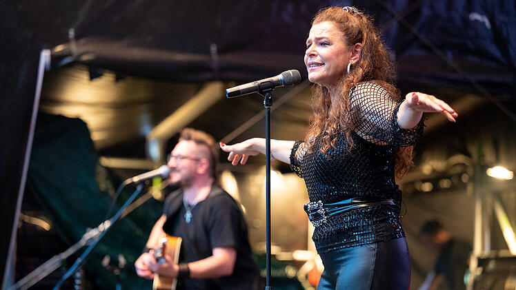 Eine S&auml;ngerin performt auf einer B&uuml;hne beim Blues- und Jazzfestival in Bamberg. Ein Gitarrist im Hintergrund begleitet sie. Die Atmosph&auml;re ist lebendig und festlich.