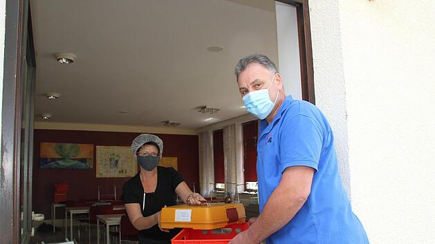 Isolde Ploner &uuml;bergibt ein Men&uuml; in der Transportbox an Fahrdienstleiter Werner Hauck. Der Koordiniert den Lieferservice "Essen auf R&auml;dern", den die Arbeiterwohlfahrt in Ebern nach wie vor anbietet. Fotos: Sven D&ouml;rr&nbsp;