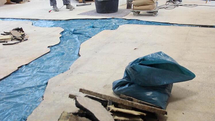 Zwei Bodenleger gießen die Lücken zwischen dem Asphaltestrich mit Epoxitestrich aus. Dort, wo vorher Wände im Hainer Kulturhaus standen oder der Asphalt weggebröckelt war, wurde blaue Folie auf den Beton gelegt, damit der neue Estrich nicht festklebt. Wenn diese Reparatur beendet ist, wird der Boden noch mit Gewebe gespachtelt. Dann kommt der Belag drauf. Die Hainer Bürger bringen am Samstag die Platten in der abgehängten Decke an.  Foto: Friedwald Schedel
