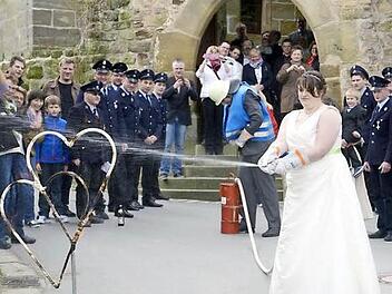 Manuela und Herbert Schmidt demonstrieren nach der Trauung in der Veitlahmer Kirche Feuerwehr-Grundkenntnisse. Die Übung klappt wie am Schnürchen - kein Wunder, der Bräutigam ist ja Kommandant der Freiwilligen Feuerwehr Schimmendorf. Foto: martinrehm.com