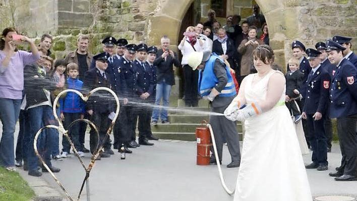 Manuela und Herbert Schmidt demonstrieren nach der Trauung in der Veitlahmer Kirche Feuerwehr-Grundkenntnisse. Die Übung klappt wie am Schnürchen - kein Wunder, der Bräutigam ist ja Kommandant der Freiwilligen Feuerwehr Schimmendorf. Foto: martinrehm.com