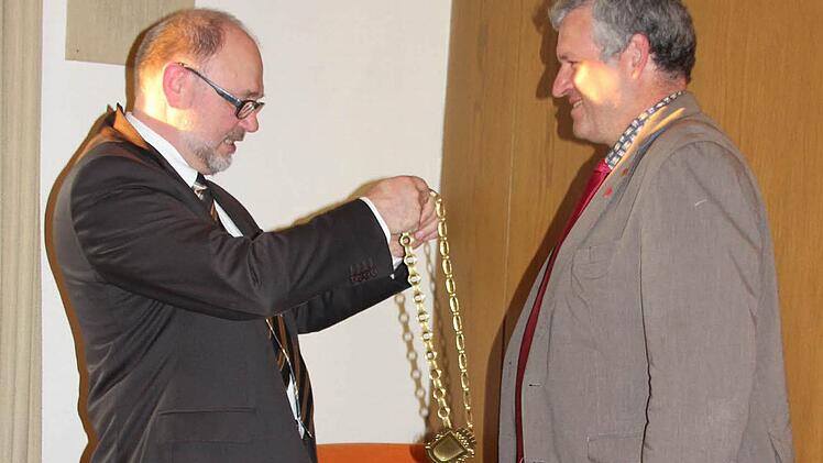 Bürgermeister Robert Herrmann (CSU) hängt seinem Nachfolger Jürgen Hennemann (SPD) die Amtskett um.