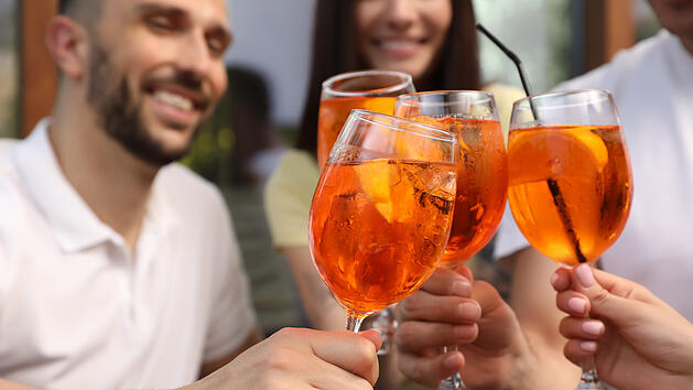 Mehrere Personen sto&szlig;en gemeinsam mit einem Aperol-Spritz an. Mittlerweile gibt es neben dem Original von Campari auch zahlreiche g&uuml;nstigere Alternativen.