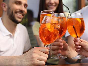 Mehrere Personen stoßen gemeinsam mit einem Aperol-Spritz an. Mittlerweile gibt es neben dem Original von Campari auch zahlreiche günstigere Alternativen.