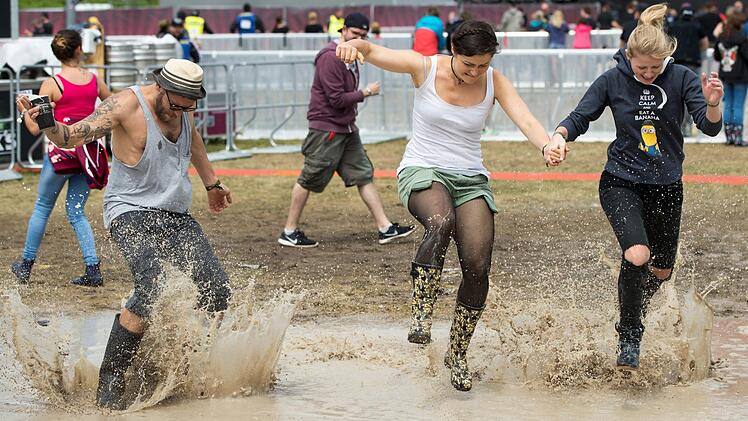 Besucher von Rock im Park springen am 04.06.2017 in Nürnberg (Bayern) durch eine Pfütze auf dem Festivalgelände. Foto: Daniel Karmann/dpa
