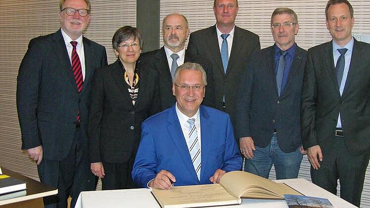 Innenminister Herrmann macht seinen Eintrag ins goldene Buch beim Festakt. Die geladenen Gäste, Bürgermeister und Landrat schauen ihm dabei zu. Foto: Klaus Oelzner
