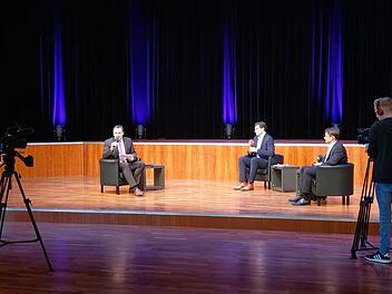 Moderator Frank Ebert (links) spricht in die Kamera, die Kandidaten Dominik Sauerteig (Mitte, rote Socken) und Christian Meyer (rechts, schwarze Socken) sitzen ihm im menschenleeren Kongresshaus gegenüber. Die Aufzeichnung des Talks ist online bei itv-coburg.de zu finden. Foto: Simone Bastian