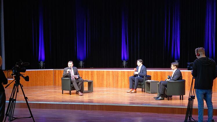 Moderator Frank Ebert (links) spricht in die Kamera, die Kandidaten Dominik Sauerteig (Mitte, rote Socken) und Christian Meyer (rechts, schwarze Socken) sitzen ihm im menschenleeren Kongresshaus gegenüber. Die Aufzeichnung des Talks ist online bei itv-coburg.de zu finden. Foto: Simone Bastian