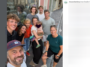 Eine Gruppe von Menschen posiert l&auml;chelnd in der N&auml;he eines neuen Outdoor-Gesch&auml;fts im Bamberger Zentrum. Eine Person h&auml;lt ein Kind im Arm. Stimmung ist fr&ouml;hlich und entspannt.