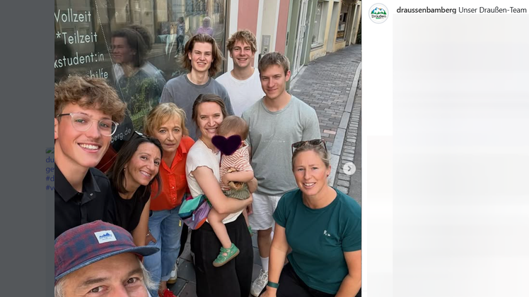 Eine Gruppe von Menschen posiert l&auml;chelnd in der N&auml;he eines neuen Outdoor-Gesch&auml;fts im Bamberger Zentrum. Eine Person h&auml;lt ein Kind im Arm. Stimmung ist fr&ouml;hlich und entspannt.