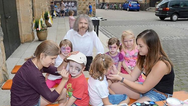Pater Helmut Haagen (Hintergrund) hatte große Freude an den Aktivitäten seiner Schäflein während der Kirchweihtage. Er trug selbst mit einer gewieften Predigt zur Unterhaltung bei und erhielt dafür viel Applaus in der Herz-Jesu-Kirche. Vorne schminken Julia Neubauer (links) und Celina Suffa (rechts) zwei tüchtige Nachwuchskräfte der Pfarrei. Foto: Karl-Heinz Hofmann