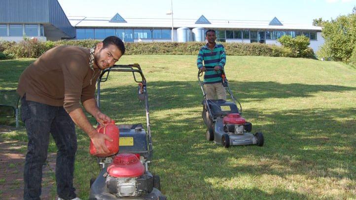 Der Syrer Ghiyath (21, links) und Gere (45) aus Eritrea mähen den Rasen im Garten der Therme Natur.Helke Renner