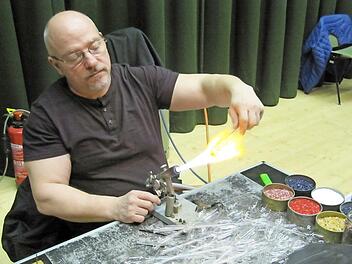 Über der Gasflamme erhitzt Udo Gering einen Rohling. Am Bildrand rechts steht farbiges Glasgranulat. Foto: Monika Schütz