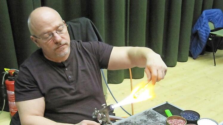 Über der Gasflamme erhitzt Udo Gering einen Rohling. Am Bildrand rechts steht farbiges Glasgranulat. Foto: Monika Schütz
