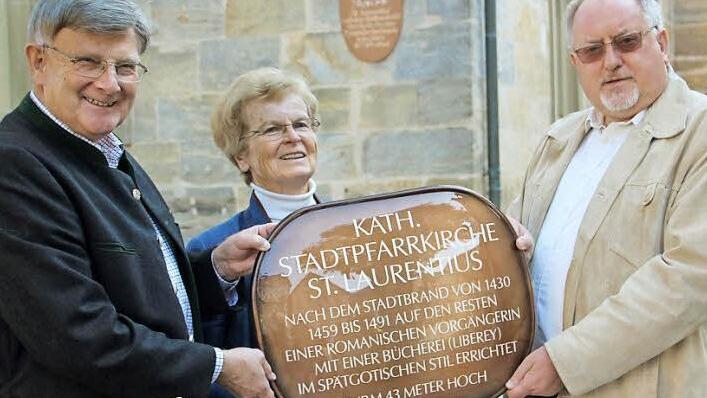 Wenn es um die geschichtlichen Belange im Altlandkreis Ebern geht, gerät Günter Lipp (links mit Ehefrau Beate) beim Erzählen schnell in Fahrt. Pfarrer Pater Rudolf Theiler dagegen machte es bei der Übergabe der neuen Denkmaltafel kurz. Er sagte, "Vielen Dank". Im Hintergrund: Das alte Schild am Liberey-Vorbau der Kirche hat nach 40 Jahren ausgedient. Foto: Eckehard Kiesewetter