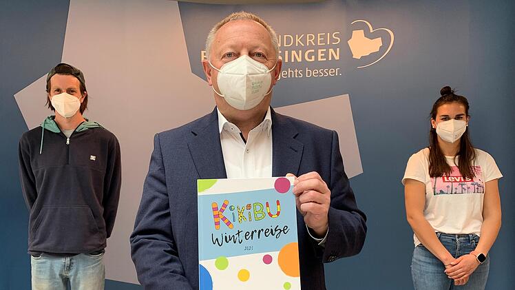 Landrat Thomas Bold (Mitte) zeigt eines der B&uuml;cher "Winterreise 2021", die Manuel M&uuml;ller (links) und Ulrike Abersfelder (rechts) vom KiKiBu-Team mit Kindergartenkindern gestaltet haben.  Foto: Anja Vorndran