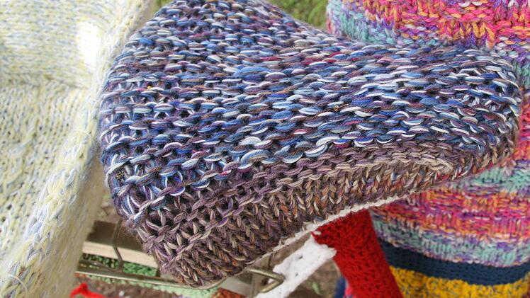 Weiche Wolle umhüllt den Fahrradsattel, bunt präsentiert sich der Baumstamm.