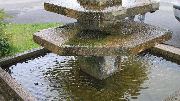 Helga Völker und Georg Fleischmann betrachten den Kalksandsteintrog, der noch heuer an der Stelle des bisherigen Brunnens aufgestellt werden soll. Foto: Matthias Einwag
