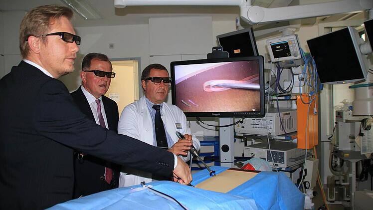 Chefarzt Dr. Boris Kardziev (rechts) und der leitende Oberarzt Dr, Aljaž Hojski (links) demonstrieren Bezirkstagspräsident Erwin Dotzel die videoassistierte Thoraxchirurgie an einer Versuchspuppe. 3D-Brillen sorgen für eine dreidimensionale Darstellung am Bildschirm. Foto: Beudert