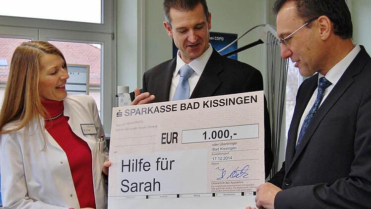 Einen Spendenscheck über 1 000 Euro überreichten Cornelia Pape, Leitende Oberärztin der Klinik am Kurpark, und der kaufmännische Leiter Holger Metz (Mitte) an Auras Bürgermeister Thomas Hack für die an Leukämie erkrankte Sarah in Aura. Foto: Dobschütz