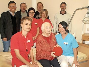 Liebevoll kümmert sich Praktikant Matthew Watson (sitzend links) zusammen mit Stefanie Melinat (rechts), um die Bewohnerin Adelgunde Weiß. Mit im Bild (stehend von links) Bürgermeister Jens Korn, Wolfgang Köhlmann, Birgit König, Rob Smith, Corinna Pfeifer und Heimleiter Bernd Robitschko. Foto: Susanne Deuerling