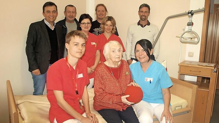 Liebevoll kümmert sich Praktikant Matthew Watson (sitzend links) zusammen mit Stefanie Melinat (rechts), um die Bewohnerin Adelgunde Weiß. Mit im Bild (stehend von links) Bürgermeister Jens Korn, Wolfgang Köhlmann, Birgit König, Rob Smith, Corinna Pfeifer und Heimleiter Bernd Robitschko. Foto: Susanne Deuerling