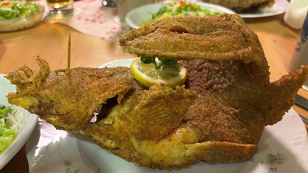 Knusprig gebratener Fisch mit Zitronenscheibe auf einem Teller, umgeben von Beilagen wie Salat. Gem&uuml;tliche Tischszene, ideal f&uuml;r Fans fr&auml;nkischer K&uuml;che.