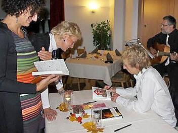 Cornelia Bartelmann und Claudia Menzel ließen die eben erworbenen Exemplare vom Autoren gleich signieren; Im Hintergrund: Franco Corleone, alias Franz Wachter aus Redwitz, der für die musikalische Umrahmung sorgte.  Foto: Ralf Kestel