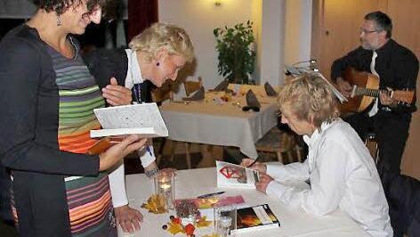 Cornelia Bartelmann und Claudia Menzel ließen die eben erworbenen Exemplare vom Autoren gleich signieren; Im Hintergrund: Franco Corleone, alias Franz Wachter aus Redwitz, der für die musikalische Umrahmung sorgte.  Foto: Ralf Kestel