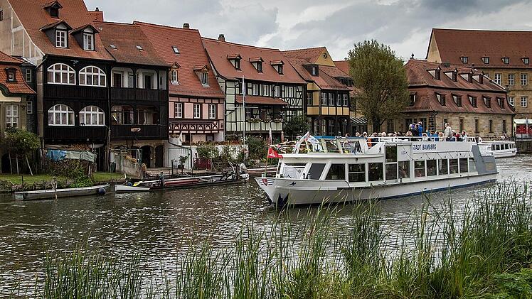 Ein Fluss mit einem Ausflugsschiff und Fachwerkhäusern im Hintergrund, typisch für malerische Städte in Franken, Deutschland.