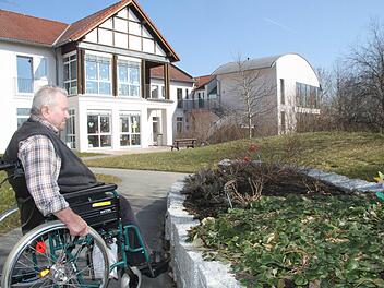 Das neue Wahrzeichen des BRK-Seniorenheims Marktleugast: der auf die Südseite verlagerte neue Haupteingang (hinten, rechts) mit der markanten Dachform. Neu angelegt ist auch der Garten mit rollstuhlgerechten Wegen, der beim Heimbeiratsvorsitzenden Robert Schott und bei seinen Mitbewohnern sehr gut ankommt. Foto: Archiv/Stephan Tiroch