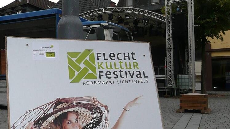 Das Plakat wirbt für das Flechtkulturfestival, dahinter  finden die Aufbauarbeiten statt.