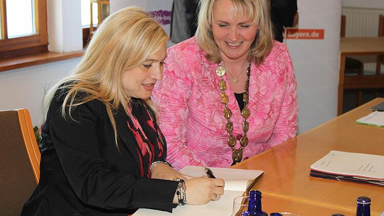 Unter den Augen von Bürgermeisterin Kathrin Heimann (r.) trägt sich Melanie Huml in das Goldene Buch der Gemeinde ein.