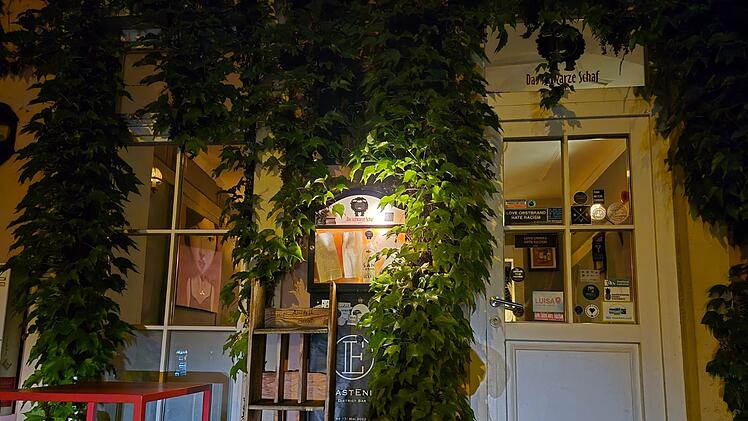 Die Eingangst&uuml;r eines Restaurants oder Caf&eacute;s ist von &uuml;ppigem Efeu umgeben. An der T&uuml;r sind verschiedene Aufkleber, und das Ganze wirkt einladend und charmant.