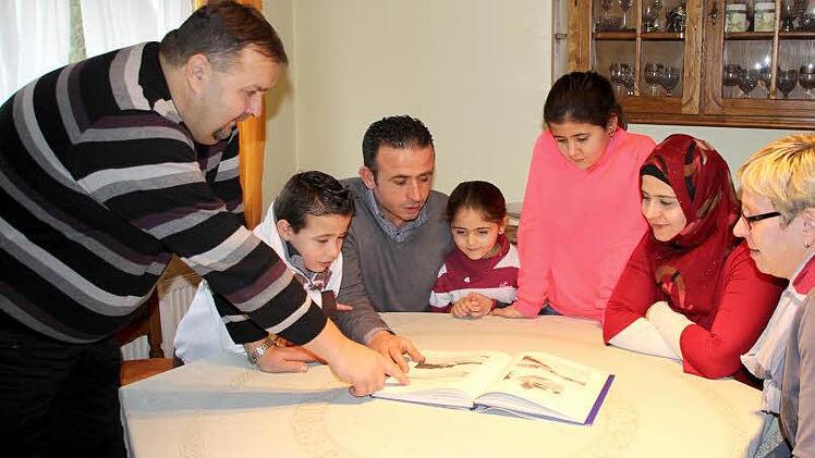 So sahen Küps und seine Ortsteile früher aus. Uwe Böhm (links) und seine Frau Silke (rechts) zeigen der Familie Alhay Mawas einen Bildband mit alten Ansichten. Asad, Mohammed, Sama, Tasmin und Diana (von links) interessieren sich für alles in ihrer neuen Heimat. Foto: Friedwald Schedel