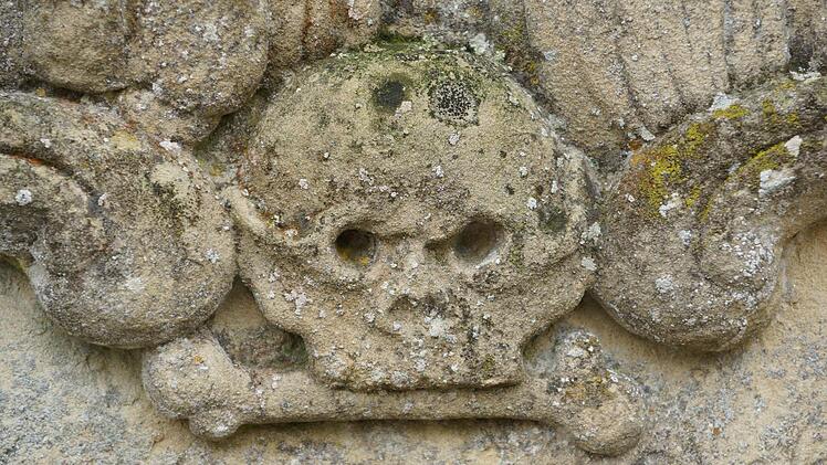 Ein Totenkopf verwittert auf einer Steinplatte.Foto: Arkadius Guzy