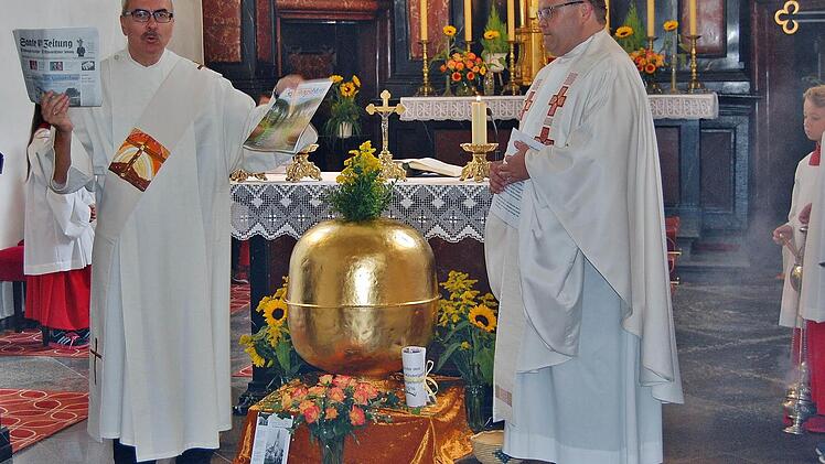 Diakon Christoph Glaser mit einer Saale-Zeitung und dem Würzburger Sonntagsblatt, die mit anderen Dokumenten und Münzen in die Turmkugel kommen; rechts: Pfarrer Gerd Greier vor der Segnung der Turmkugel.  Foto: Sigismund von Dobschütz