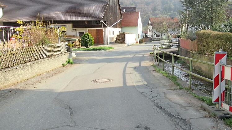 Der Blick aus Richtung Hundshaupten in die Ortsmitte von Oberzaunsbach zeigt den schlechten Fahrbahnzustand und die erneuerungsbedürftige Bachmauer.