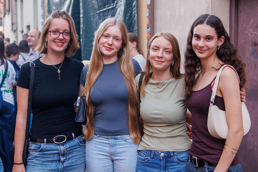 Vier junge Frauen posieren l&auml;chelnd f&uuml;r die Kamera bei der Bamberger Sandkerwa 2026. Im Hintergrund sind weitere Menschen in Feierlaune zu sehen.