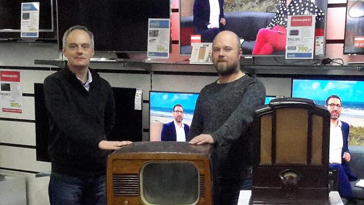 Junge Chefs mit historischen Geräten: Ralph und Mathias Knüttel (rechts) holen immer wieder einmal den alten Fernseher und das urige Radio hervor. Beide Objekte stammen noch aus der Anfangszeit des Bad Brückenauer Traditionsunternehmens. Foto: Rolf Pralle
