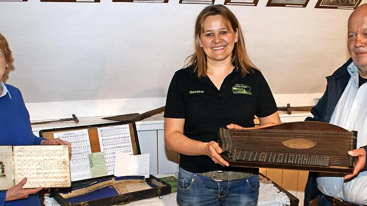 Peter Becker (rechts) überreicht an Vorsitzende Bettina Rubel (Mitte) einen besonderen Schatz: Die Zither aus dem Jahr 1889 und die Noten aus dem Jahr 1884, die Lucina Spitzenpfeil entgegennehmen durfte, sind ein weiteres historisches Highlight im kleinen Heimatmuseum in der Zecher-Halle in Neukenroth. Foto: Joachim Beez