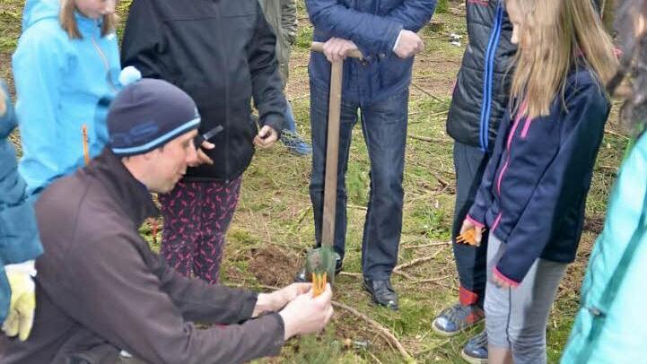 Baumfachmann Michael Weißerth setzt einem Bäumchen eine Krone auf, die es vor Wildverbiss schützen soll. Die jungen Stockheimer und Bürgermeister Rainer Detsch (Freie Wähler)passen gut auf. Foto: K.-H. Hofmann